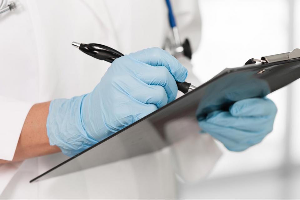 Medical staff member wearing gloves and writing on clipboard